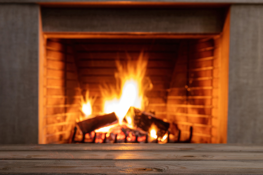 Table on blur burning fireplace background. Empty wooden planks, space. Winter holidays cozy warm home, Christmas, New Year dinner table template.<br />
